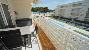Een balkon met een tafel en stoelen, uitkijkend op een zwembadgedeelte met ligbedden en een gebouw met balkons.