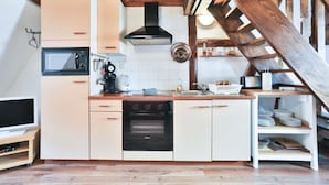 Cocina compacta con microondas, horno y cafetera. Una escalera de madera conduce a un altillo con vistas.