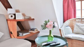 Una sala de estar acogedora con una mesa redonda, un florero con flores, un control remoto y una silla de mimbre.