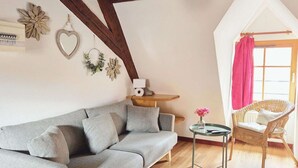 Un salón acogedor con un sofá gris, un sillón de mimbre y una pequeña mesa con un florero.
