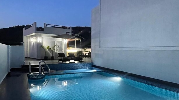 Una piscina en la azotea con superficie de agua azul cristalina, rodeada por un edificio moderno de techo plano y pared exterior blanca.