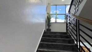 Una escalera con escalones de mármol negro y franjas de seguridad amarillas, que conduce a una plataforma con vista al cielo a través de una ventana.