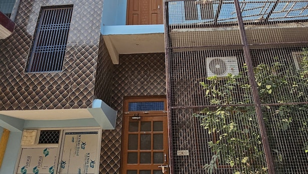 Un edifici residencial de diverses plantes amb façanes de maó i estuc, una entrada destacada amb una porta de fusta i una petita zona de jardí amb una tanca metàl·lica.