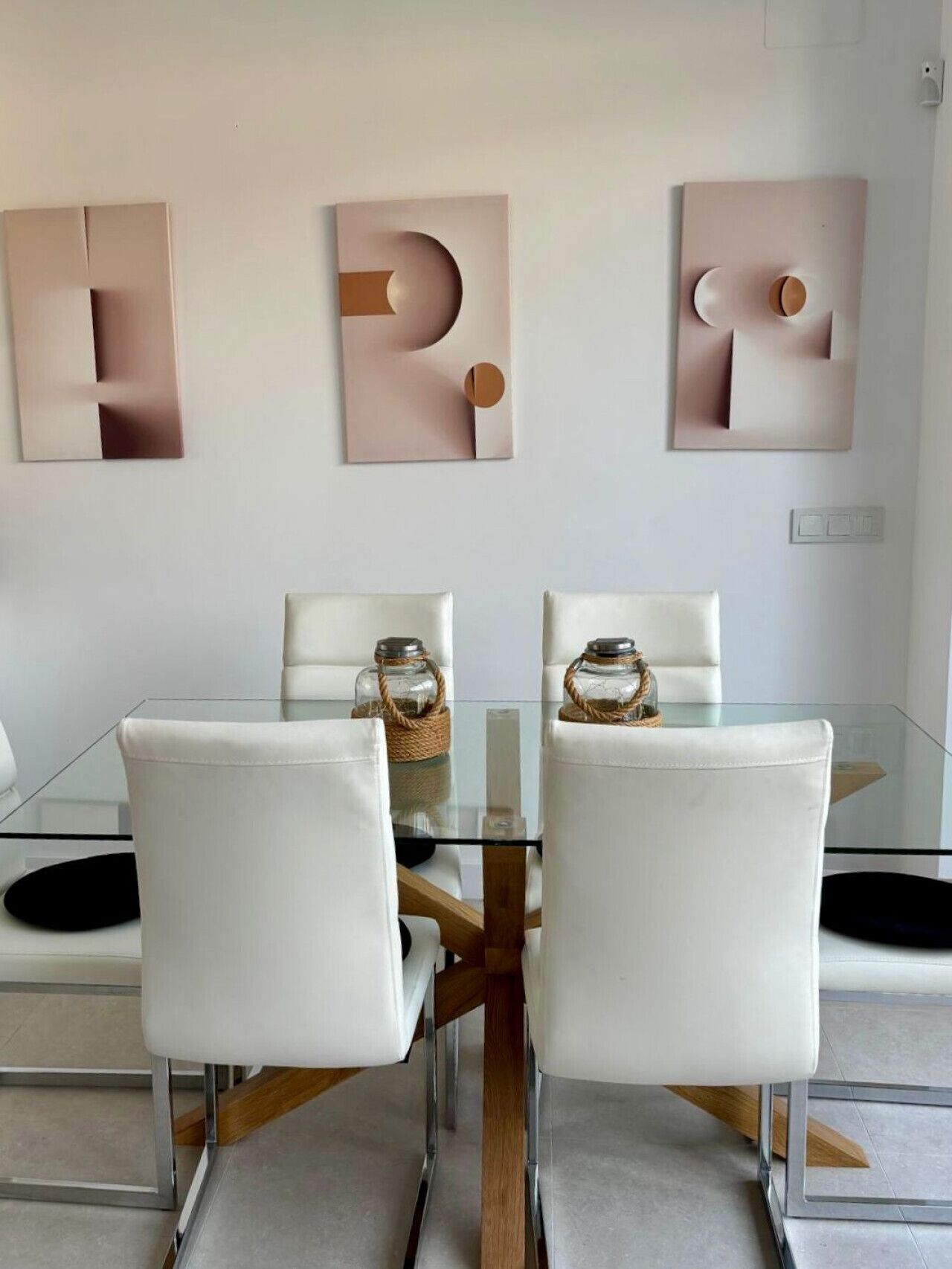 A dining area with a glass table, white chairs, and abstract wall art.