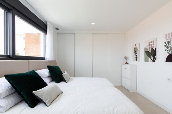 Un dormitorio moderno con una cama grande, ropa de cama blanca y almohadas verdes. Se ve una ventana con vistas a un edificio.