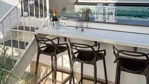A balcony with a bar area, chairs, and a view of the ocean.