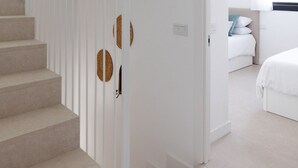 A modern interior with a staircase, a bedroom with a bed and a nightstand, and a bathroom with a bathtub.