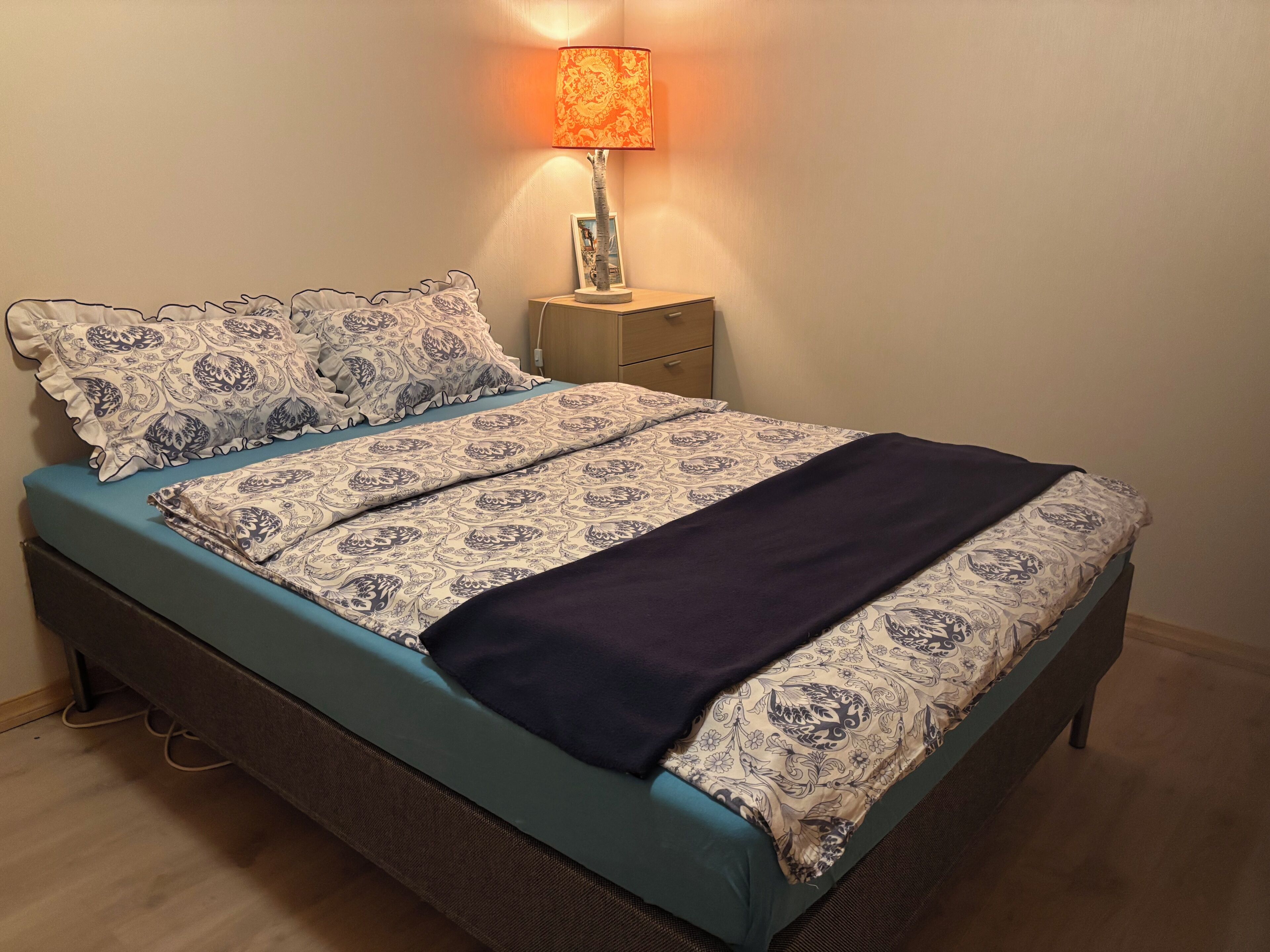 Un lit avec une couvre-lit à motifs et des oreillers, une lampe de chevet et une table de chevet en bois.