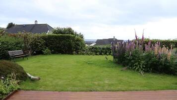 Een tuin met een houten terras, een bank en diverse planten.