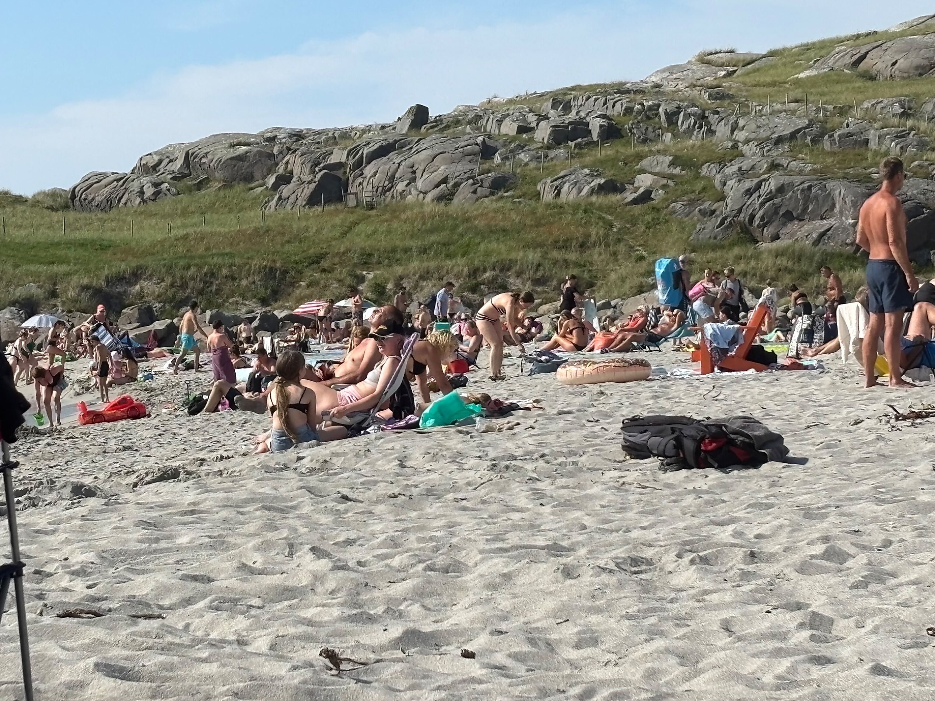 Une plage bondée où les gens se prélassent au soleil et se promènent.