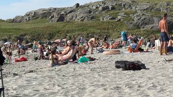 Une plage bondée où les gens se prélassent au soleil et se promènent.