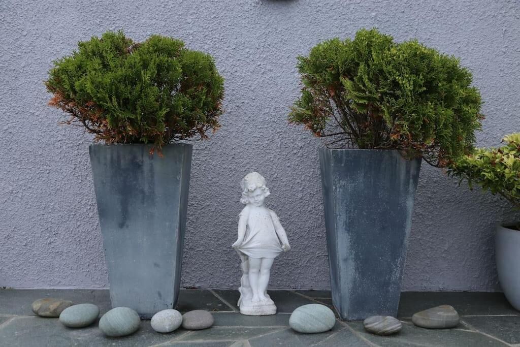 Two large grey planters with small trees and a white statue between them.
