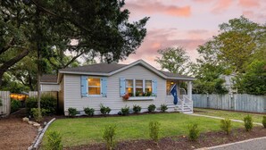 A single-story house with a front porch, a small front yard with young trees, and a wooden fence in the background.