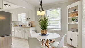A modern kitchen with white cabinetry, a central island with chairs, a hanging light fixture, and a potted plant.