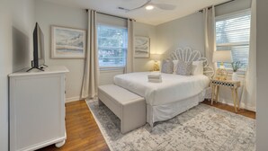 A bedroom with a bed, a bench, a TV, a ceiling fan, and artwork on the walls.