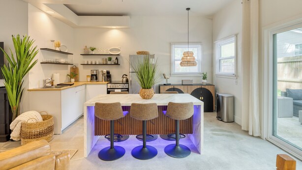 A modern kitchen with a central island, bar stools, and a large potted plant.