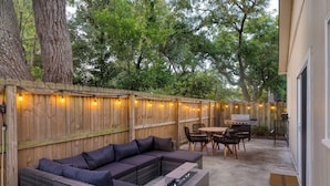 An outdoor patio with a sectional sofa, a table with chairs, a grill, and string lights.