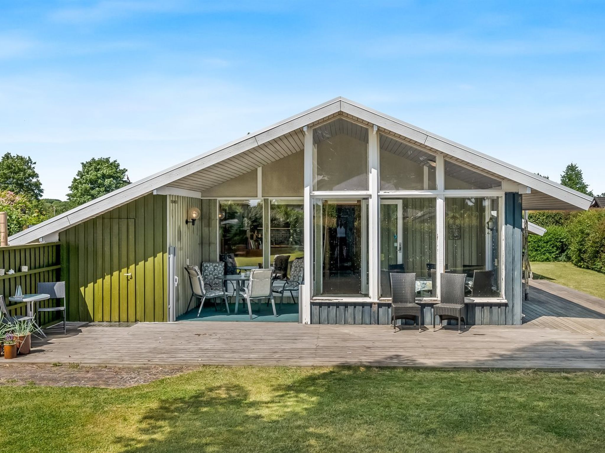 Ein modernes Haus mit einer großen Terrasse, einer überdachten Veranda und einem gläsernen Wohnbereich.