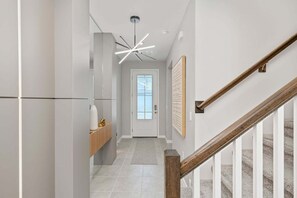 A modern hallway with a wooden bench, a ceiling light fixture, and a staircase with wooden railings.