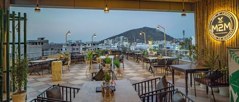 A rooftop cafe with outdoor seating, a view of the city, and a mountain in the background.