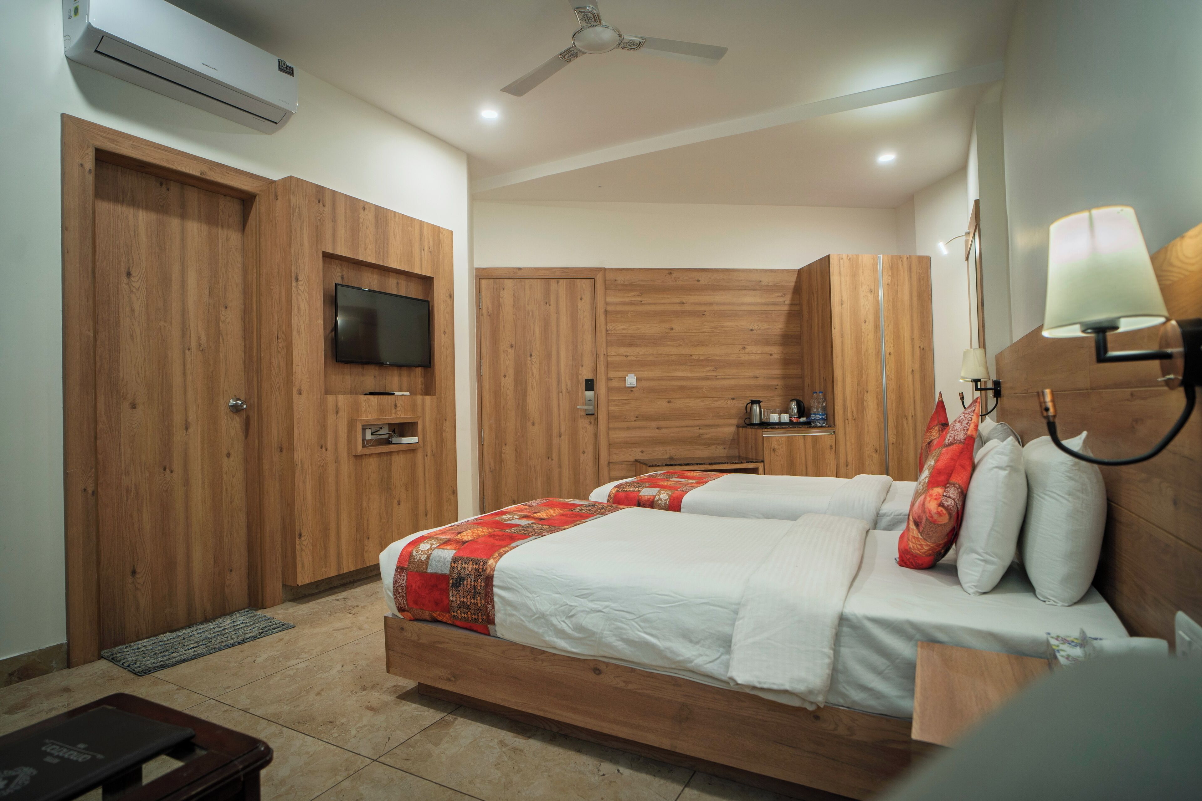 A bedroom with two beds, wooden wardrobes, a television, and a ceiling fan.