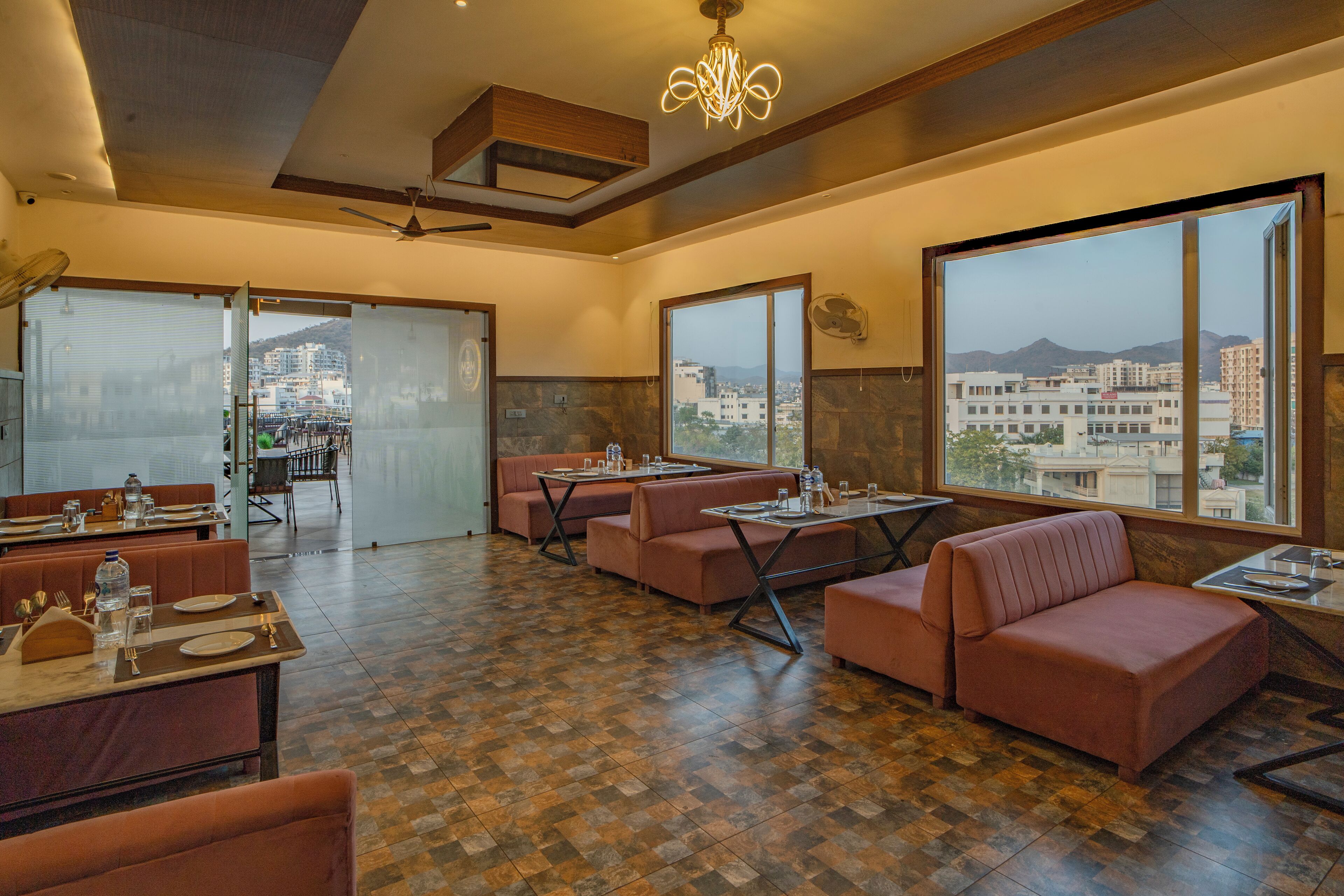 A spacious dining area with multiple seating options, including booths and tables, and large windows offering a view of the cityscape.