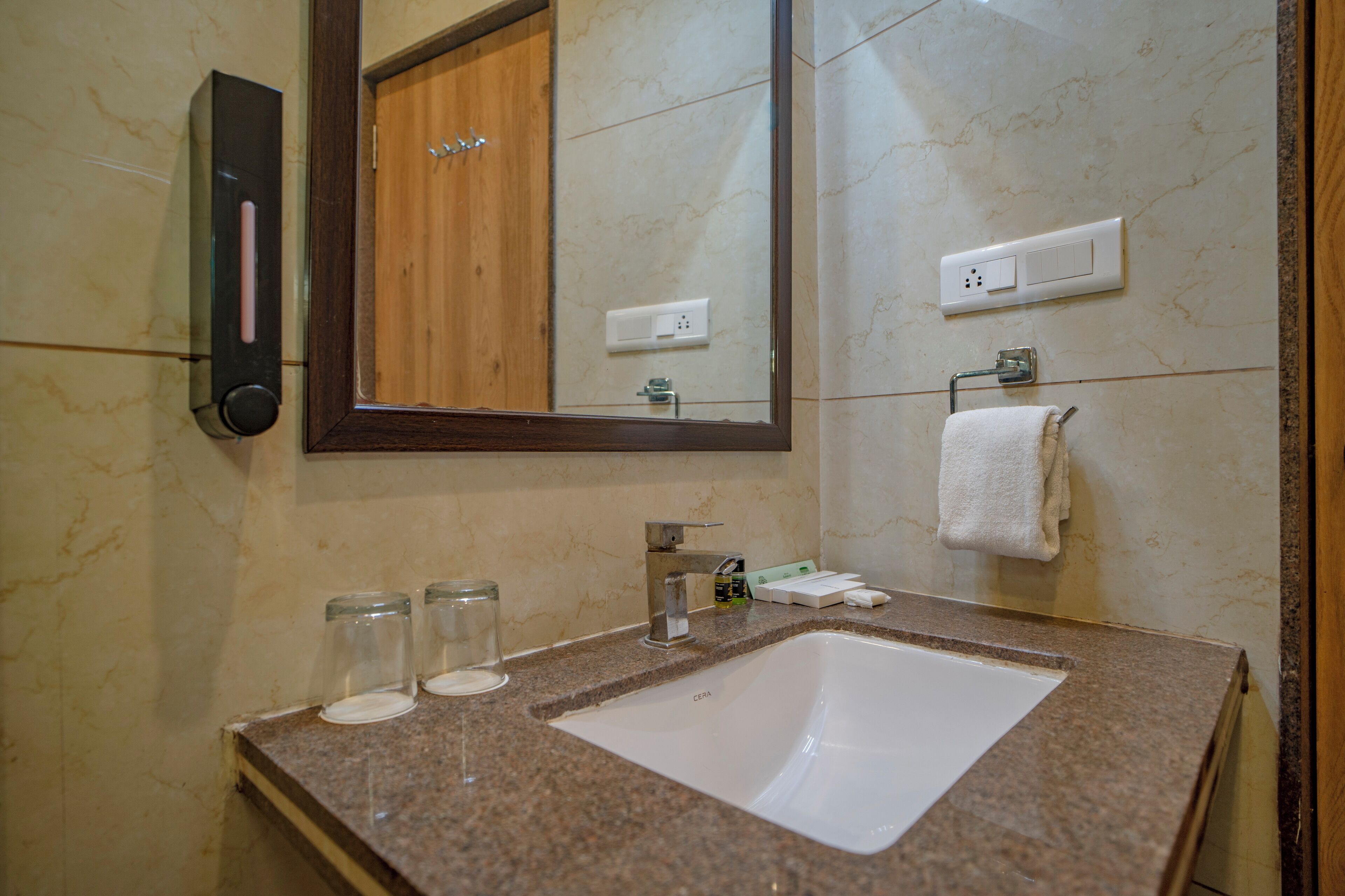 A bathroom with a granite countertop, a white sink, a mirror, a wooden door, and a towel hanging on the wall.