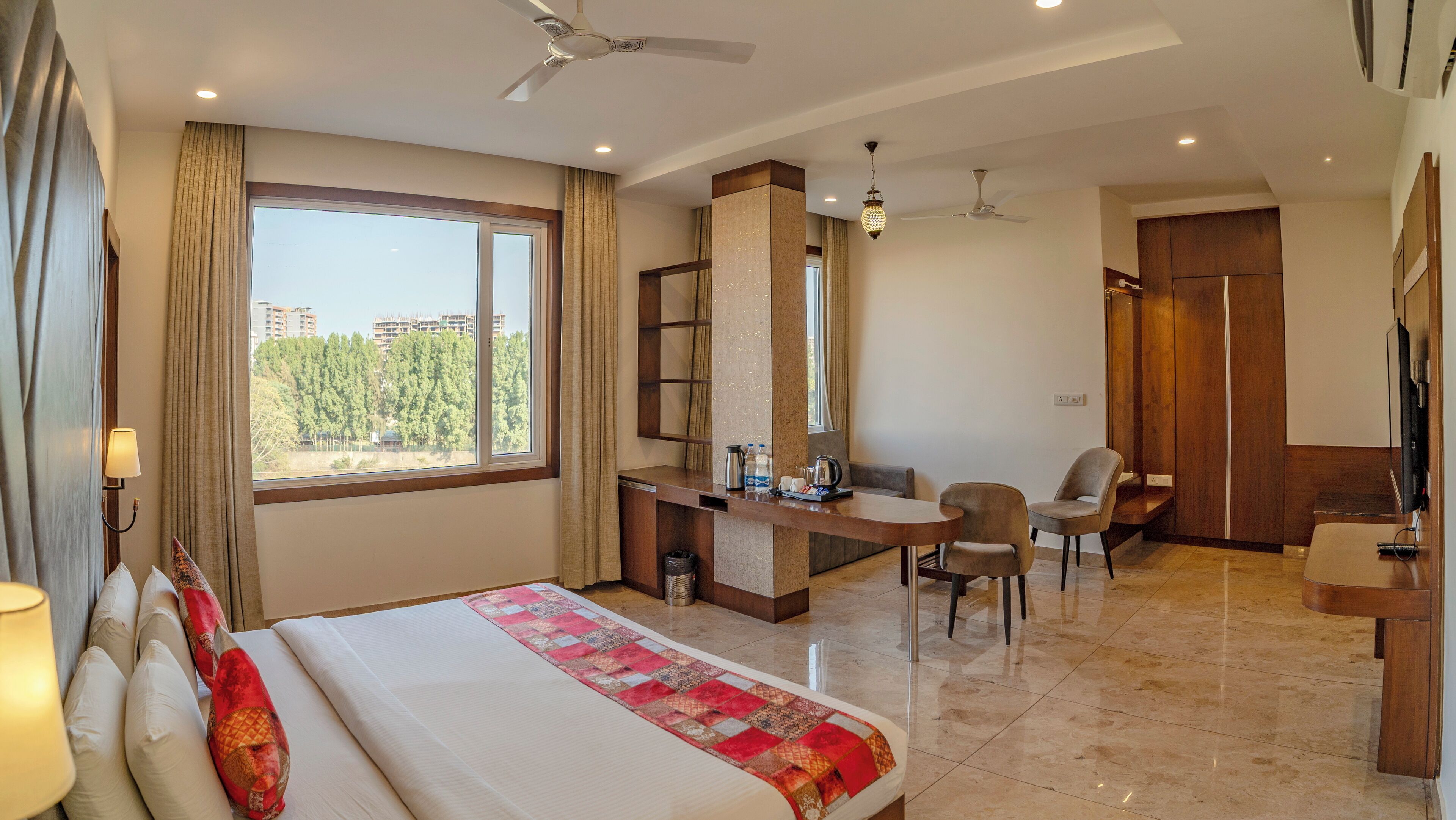 A hotel room with a bed, desk, chairs, and a TV.