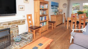 Un salon chaleureux avec une cheminée, une bibliothèque, un coin repas avec des meubles en bois et un téléviseur fixé au mur.