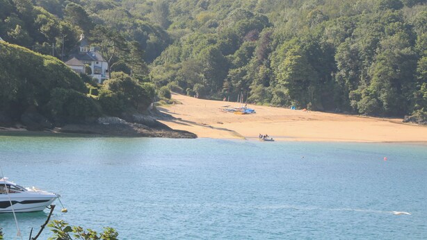 Un paysage côtier avec une plage de sable, un bateau et une maison entourée d’une forêt dense.