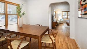 A dining area with a wooden table and chairs, a vase with a plant, and a view through an archway to a living room with a sofa and a TV. - 5 min drive to CU/Pearl - Best Neighborhood (Boulder)