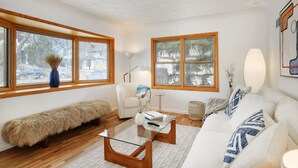A modern living room with a white sofa, a glass coffee table, a fur bench, and two windows with wooden frames. - 5 min drive to CU/Pearl - Best Neighborhood (Boulder)