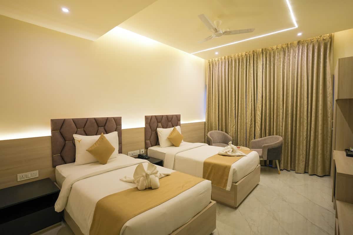 A hotel room with two beds, a desk, a chair, a ceiling fan, and a large window with curtains.
