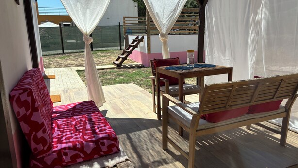 A covered outdoor seating area with a wooden bench and a table, a cushioned bench with a patterned cover, and a staircase leading to an upper level. - Herdade Palma T1p (country house) (Moita)