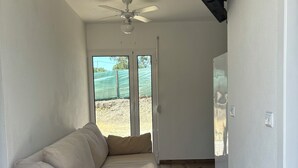 A room with a beige sofa, a ceiling fan, a flat-screen TV mounted on the wall, and a sliding glass door leading to an outdoor area. - Herdade Palma T1p (country house) (Moita)