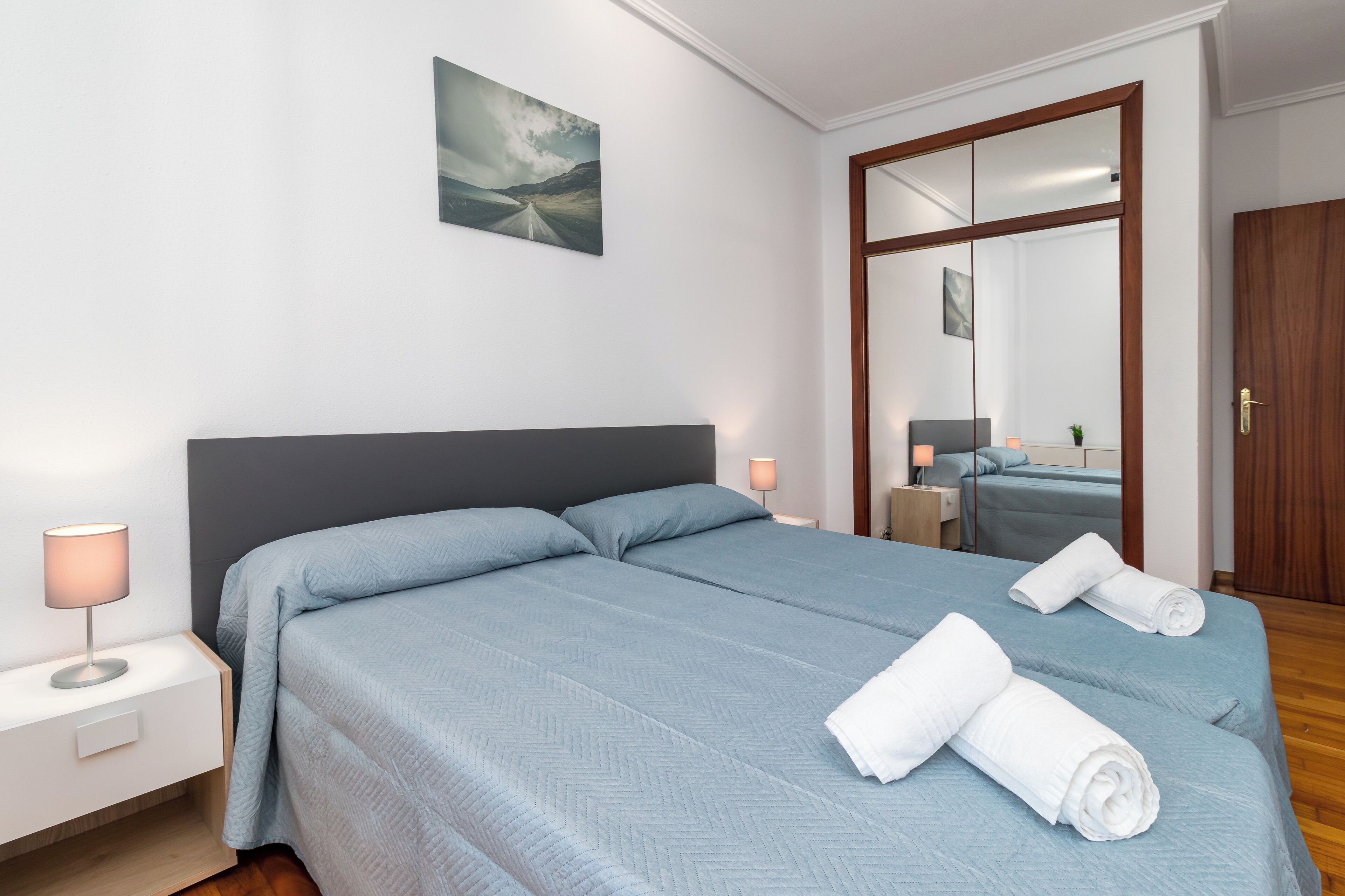 Une chambre d’hôtel avec un grand lit, une table de chevet avec une lampe, un miroir et une vue sur l’extérieur.