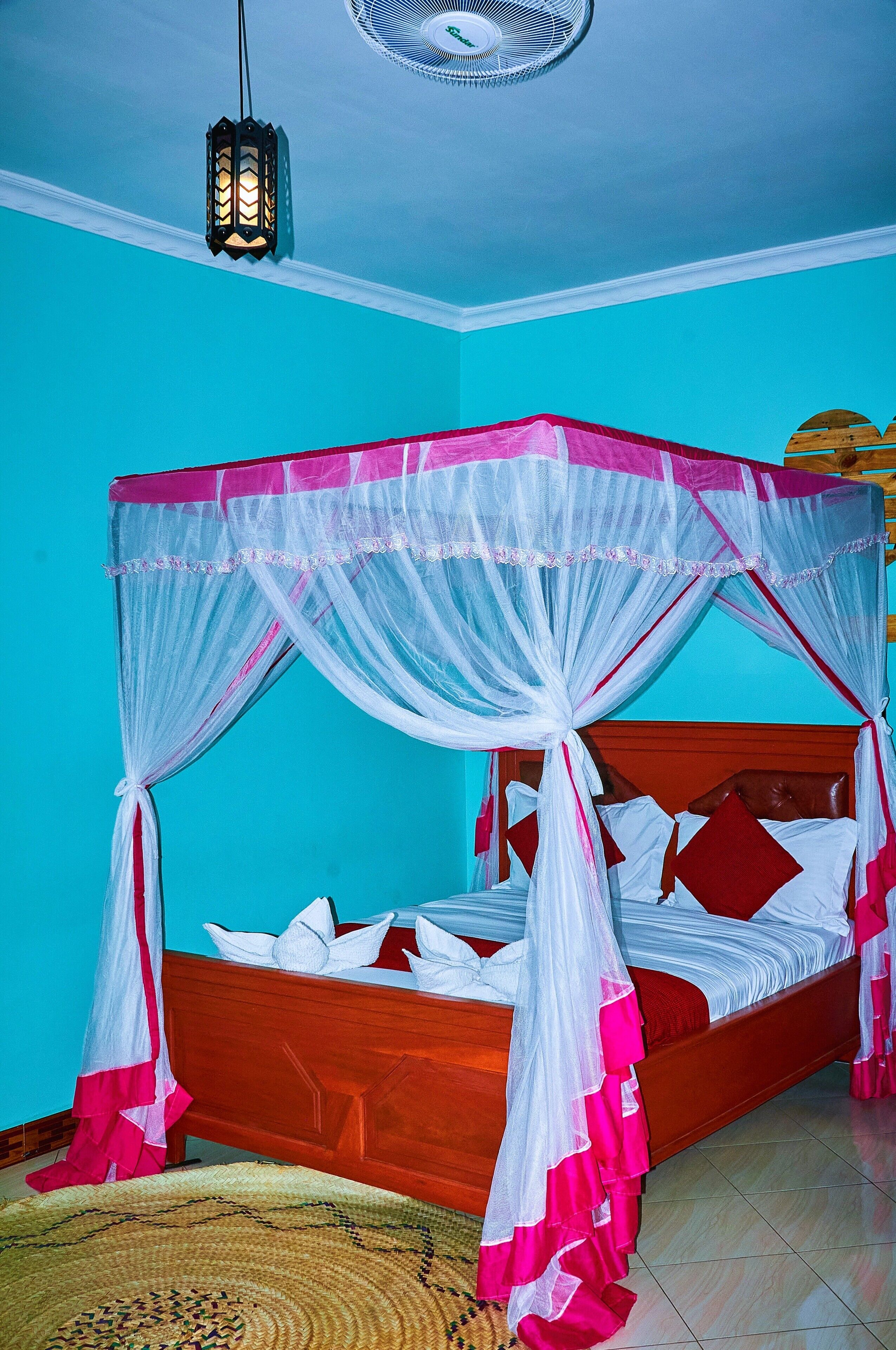 A room with a bed under a canopy, a ceiling fan, and a wall-mounted light fixture.