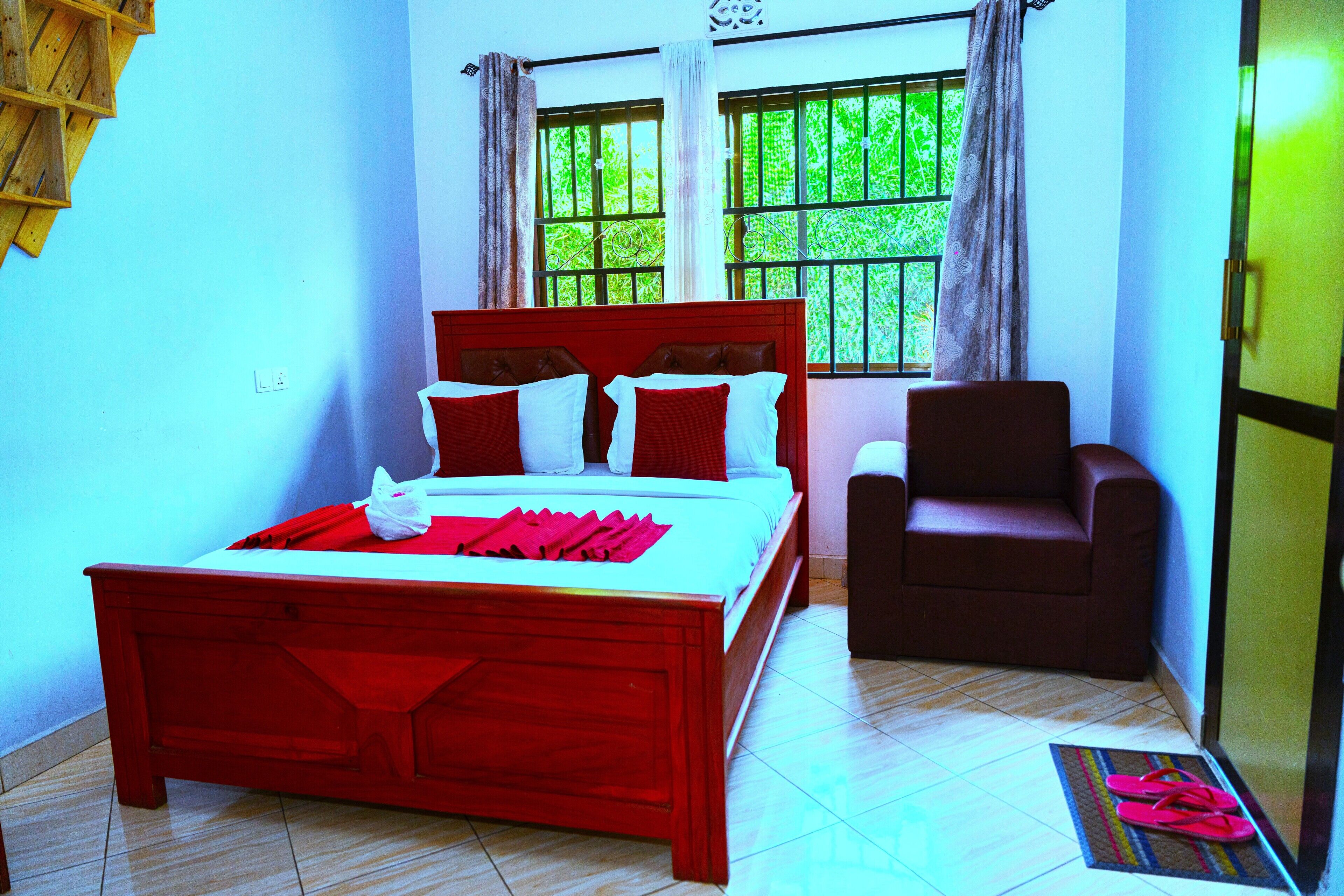 A room with a bed, a chair, a window with curtains, and a door.