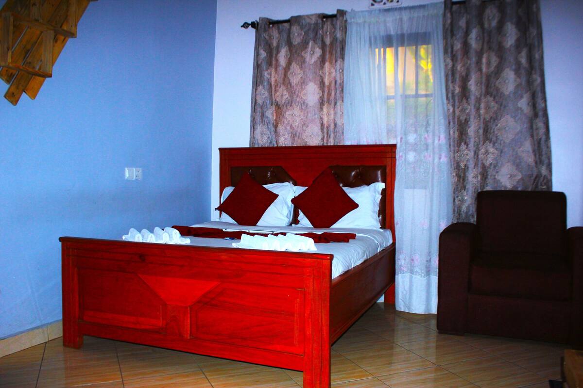 Ein rotes hölzernes Bett mit weißen und roten Kissen in einem Zimmer mit blauen Wänden und einer Holzbalkendecke.