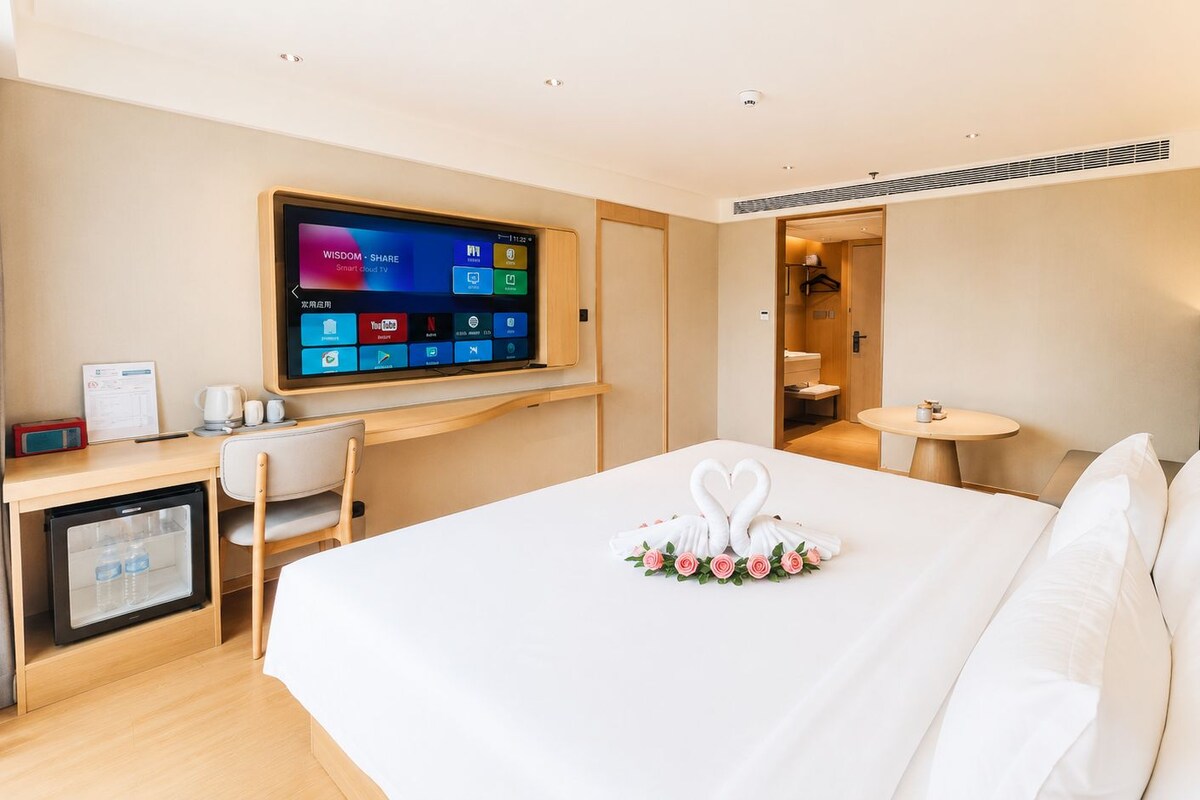 A hotel room with a bed, a desk with a computer, a television, and a small refrigerator.