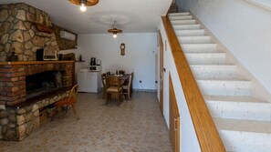 A cozy living area with a stone fireplace, a dining table with chairs, a kitchen area with appliances, and a wooden staircase.