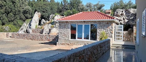 A stone house with a red-tiled roof, a stone wall, and a paved driveway.