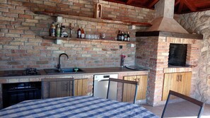 Uma cozinha com parede de tijolos, pia, lava-louças e churrasqueira.