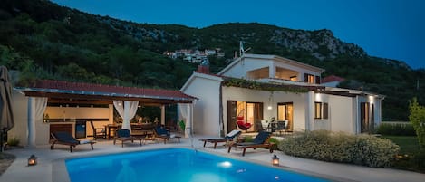 Una casa de dues plantes amb piscina, zona d'estar a l'exterior i vistes als turons del voltant.