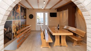Un restaurante con bancos de madera, una mesa larga, paredes de piedra y un ventanal grande.
