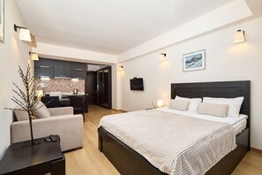 A modern hotel room with a large bed, a sitting area with a sofa, a desk, and a kitchenette in the background. - MaRKoS Flat in Block 1, New Gudauri (Gudauri)