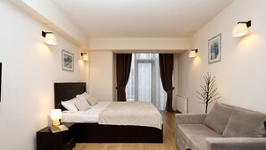 A modern hotel room with a bed, a bedside table with a lamp, a sofa, and a decorative tree. - MaRKoS Flat in Block 1, New Gudauri (Gudauri)