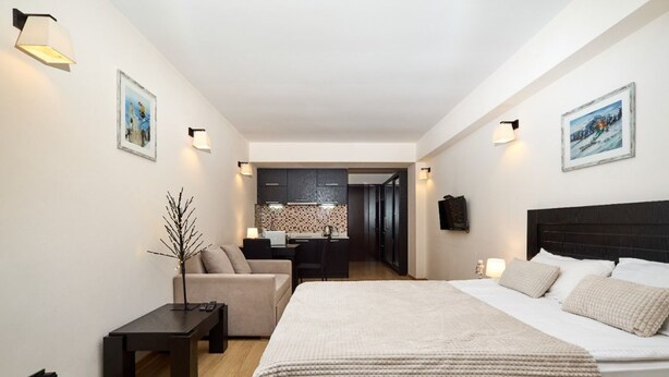 A modern hotel room with a large bed, a desk, and a sofa. There are wall-mounted lights and artwork on the walls. - MaRKoS Flat in Block 1, New Gudauri (Gudauri)
