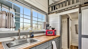 A kitchen with a large window, a sink, a red microwave, and a coffee maker.