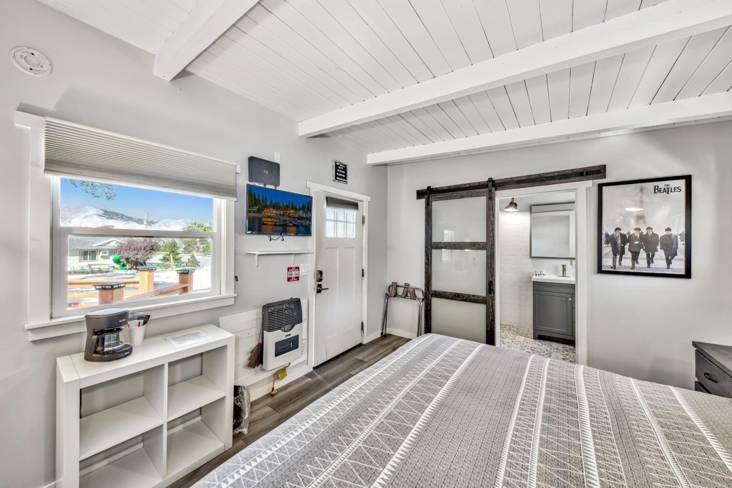 A modern hotel room with a large bed, a TV, a sliding door to a bathroom, and a window with a view of a mountain.